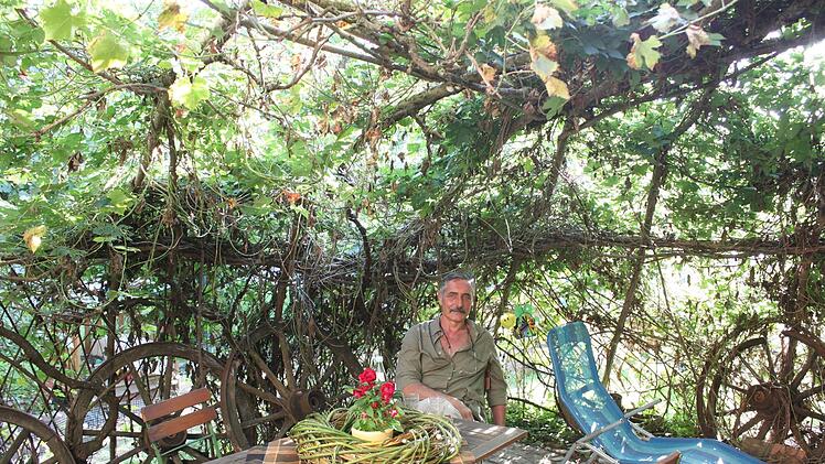 Ganz von schützendem Grün umgeben: Heinrich Geßlein sitzt in seinem Lieblingsflechtobjekt vor seinem Haus in Marktgraitz. Aus Weide geformt wie diese Pergola ist auch der Tischschmuck, ein grüner Kranz mit Blumenstock in der Mitte. Fotos: Ramona Popp