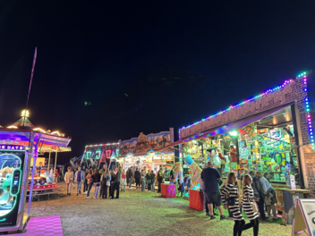 Ein nächtlicher Jahrmarkt mit bunten Lichtern, Buden und Fahrgeschäften. Menschen spazieren und genießen die festliche Atmosphäre der Gaustadter Kirchweih.
