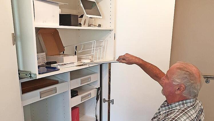 Reinhard Wolf demonstriert, wie man auch vom Rollstuhl aus leicht an die oberen Regalfächer herankommt. Der Spezialschrank hat ein patentiertes System. Per Fernbedienung kann man den oberen Schrankteil absenken.