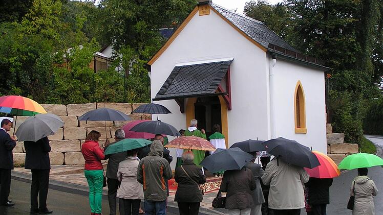 Unter Regenschirmen nahmen die Reifenberger an der Einweihung ihrer restaurierten Kapelle teil. Gefeiert wurde dann später im Feuerwehrhaus. Foto: Heidi Amon