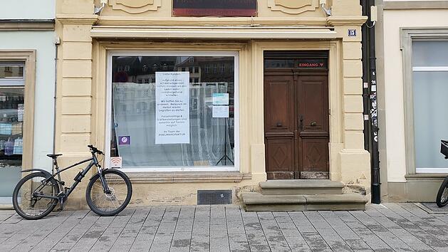 Ein geschlossenes Gesch&auml;ft mit gelber Fassade und Holzdetails in Bamberg. Ein Schild im Fenster informiert &uuml;ber die vor&uuml;bergehende Schlie&szlig;ung. Ein Fahrrad lehnt an der Fassade.