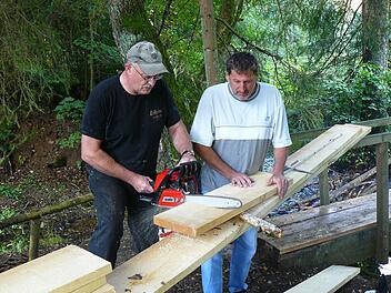Klaus Hieke und Martin Döring schneiden die Bohlen für die Brücke über den Rehbach an Ort und Stelle zu. Fotos: Sonja Adam
