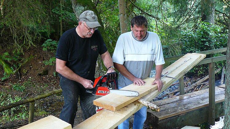 Klaus Hieke und Martin Döring schneiden die Bohlen für die Brücke über den Rehbach an Ort und Stelle zu. Fotos: Sonja Adam