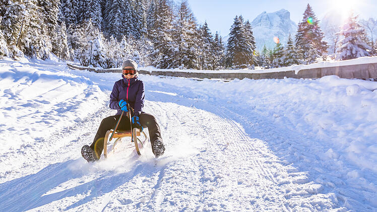 Cheerful girl riding a sled downhill, snow, sunny winter landsca