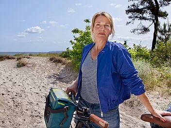 Nach der geplatzten Hochzeit mit Max musste Nora Kaminski (Tanja Wedhorn) erstmal weit weg. Doch zu Beginn des 27. Films "Praxis mit Meerblick - Willkommen zu Hause" kommt sie zur&uuml;ck auf R&uuml;gen.