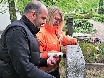 Friedhofsverwalter Stefan Krieg und Mitarbeiterin Carmen Goll pressen den Kipp-Tester an die Oberkante eines Grabsteins. Foto: Sigismund von Dobschütz