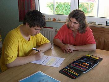 Tim Schulze sitzt zu Hause in Oberbayern am Esstisch und bearbeitet Unterrichtsmaterial, das wöchentlich  per Post aus  Bamberg kommt. Das Bild aus dem Sommer 2011 zeigt ihn mit seiner Mutter.  Foto:  privat