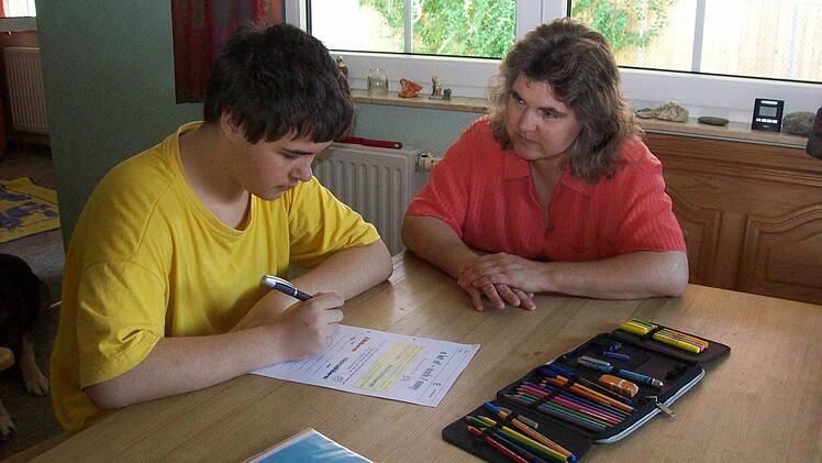 Tim Schulze sitzt zu Hause in Oberbayern am Esstisch und bearbeitet Unterrichtsmaterial, das wöchentlich  per Post aus  Bamberg kommt. Das Bild aus dem Sommer 2011 zeigt ihn mit seiner Mutter.  Foto:  privat