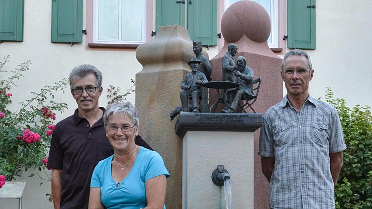 Vor dem Dorfbrunnen haben sich Schriftführer Wolfgang Mandery (von links), Vorsitzende Herta Müller und Reinholf Gabel (Spartenleiter Gartenbau) vom Heimat- und Wanderverein Aschach aufgestellt. Sie bereiten gerade das 50-jährige Vereinsjubiläum vor. Foto: Björn Hein