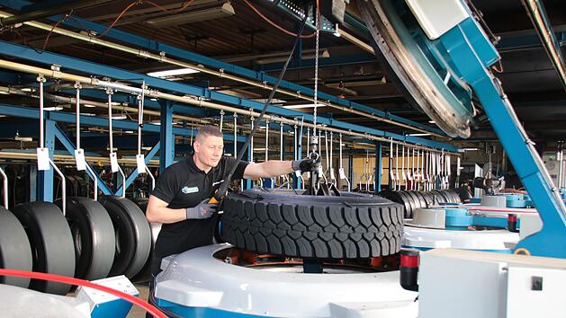 Mit einem Kran hebt ein Mitarbeiter von Reifen M&uuml;ller einen runderneuerten Reifen aus der Maschine.