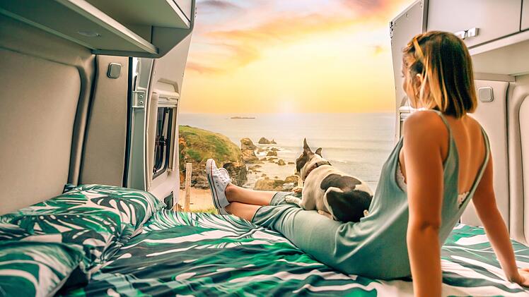 Frau mit ihrem Hund, die auf dem Bett ihres Wohnmobils sitzend den Sonnenuntergang beobachtet  Unbekannte junge Frau mit ihrem Boston-Terrier-Hund, die auf dem Bett ihres Wohnmobils sitzend den Sonnenuntergang beobachtet Woman with her dog watching the sunset sitting on the bed of her camper van  Unrecognizable young woman with her boston terrier dog watching the sunset sitting on the bed of her camper vanCamping, Campen, Wohnmobil, Wohnwagen, Urlaub, Caravan, Gas, Gaskartusche, Flasche