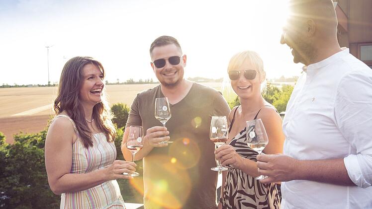 Vier Menschen trinken Wein auf einer Terrasse bei Sonnenschein