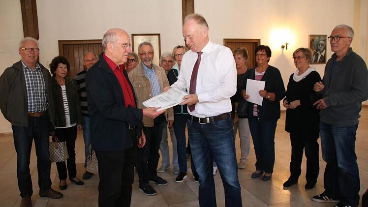 Wolfgang Blümlein (vorne links) übergibt an Bürgermeister Helmut Blank (vorne rechts) die Unterschriftenliste des Bürgerbegehrens.