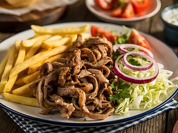 Gyrosfleisch mit Pommes Frites und Salat auf einem Teller, serviert mit Dip und Tomaten.
