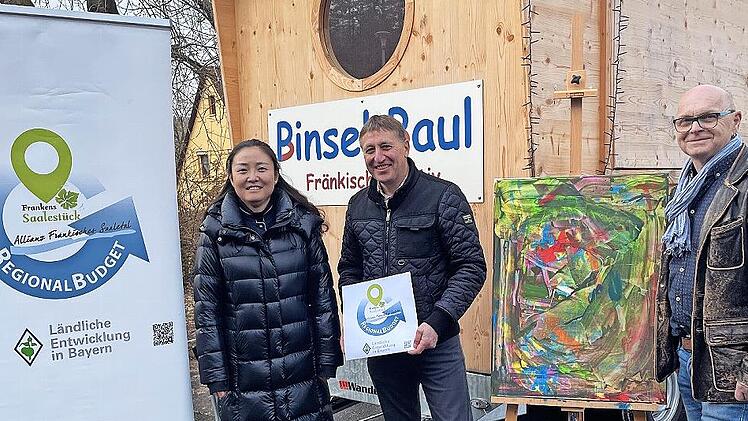 Allianzmanagerin Wenjun Zhang (v.l.), B&uuml;rgermeister Rainer Morper und Bernhard G&ouml;&szlig;mann-Schmitt vom Verein erLebenskunst freuen sich: Mit dem durch das Regionalbudget gef&ouml;rderten Anh&auml;nger bringt der Verein die Kunst in Schulen und Kinderg&auml;rten.