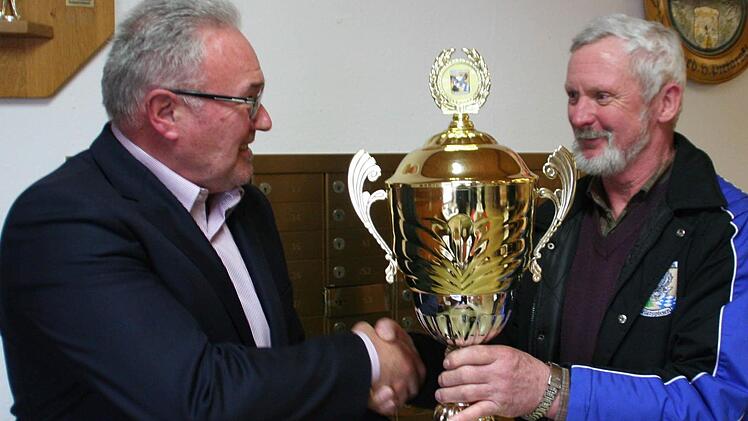 Pokal im Champions League Format für die siegreichen Schützen aus Reiterswiesen. Bürgermeister Thomas Leiner (links) gratuliert Burkard Faber.  Foto: Werner Vogel