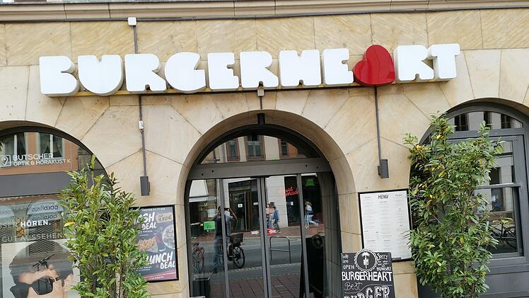Das Bild zeigt den Eingang eines Burgerheart-Restaurants. Über der Tür steht der Name, flankiert von Topfpflanzen. Ein Aufsteller bewirbt Burgerangebote.