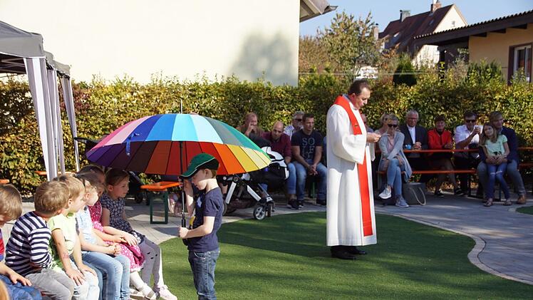 Ein großer Regenbogen-Schirm symbolisierte Gottes Schutz und Schirm, unter den Pfarrer Rusin den neuen Spielgarten und alle Kinder der Kindertagesstätte St. Magdalena in Ebelsbach stellte. Foto: Sabine Weinbeer