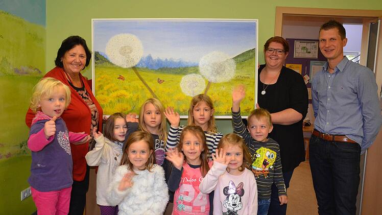 Hier im Speisezimmer der Kindertagesstätte "Pusteblume" wird das neue Pusteblumen-Bild der Malerin Ursula Cukic-Hartmann (links neben dem Bild) hängen. Darüber freuen sich neben den Kleinen auch Leiterin Janine Henschel (rechts) sowie der Vorsitzende des St.-Johannis-Zweigvereins, Christof Göbel.  Fotos: Jana Keul