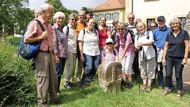 Hier posiert die Wandergruppe um Hildegard Wächter (mit der Hand am Stein) am Sühnekreuz vor der Pfarrkirche Sankt Laurentius. Foto: Mario Deller