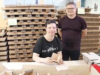 Thomas Mahr (rechts) mit Daniel Groh, einem der 65 Beschäftigten der Werkstatt Schmeilsdorf, der Transportverpackungen faltet. Bild rechts: Daniel Karnoll zeigt Hannah Stößlein seine Arbeit. Die Diakonin ist neu im Team und lernt gerade alle Arbeitsbereiche der Werkstatt kennen.   Fotos: Lena Oedinger/Jens Schuwald