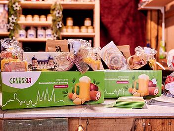Ein grünes "Genussla"-Paket mit regionalen Produkten aus Bamberg steht in einem Geschäft. Dekoriert ist es mit Geschenkbändern und weiteren weihnachtlichen Artikeln.
