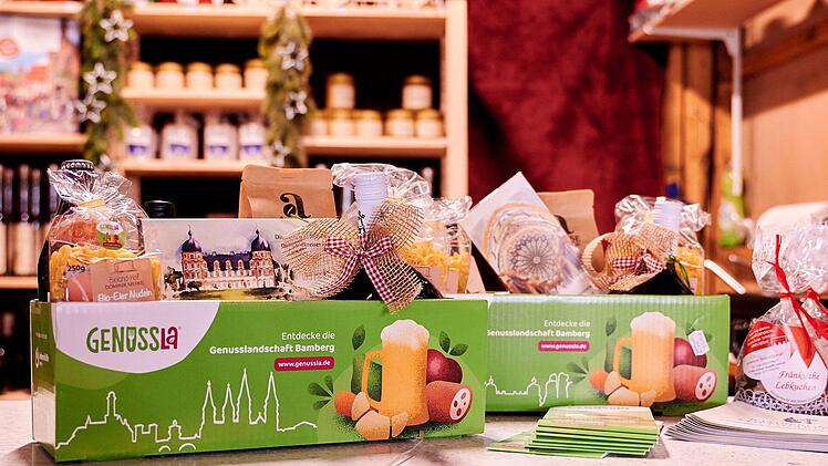 Ein grünes "Genussla"-Paket mit regionalen Produkten aus Bamberg steht in einem Geschäft. Dekoriert ist es mit Geschenkbändern und weiteren weihnachtlichen Artikeln.