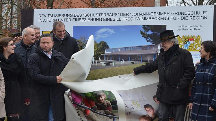 Enthüllung. Bürgermeister Martin Finzel zieht das Plakat beiseite, das bisher die Bautafel verdeckte, die über den Umbau zum Lehrschwimmbecken informiert.Rainer Lutz