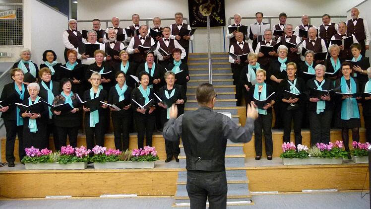 Die Frauen des Gesangvereins Weitramsdorf tragen einen türkisfarbenen Schal, die Männer eine violette Weste.