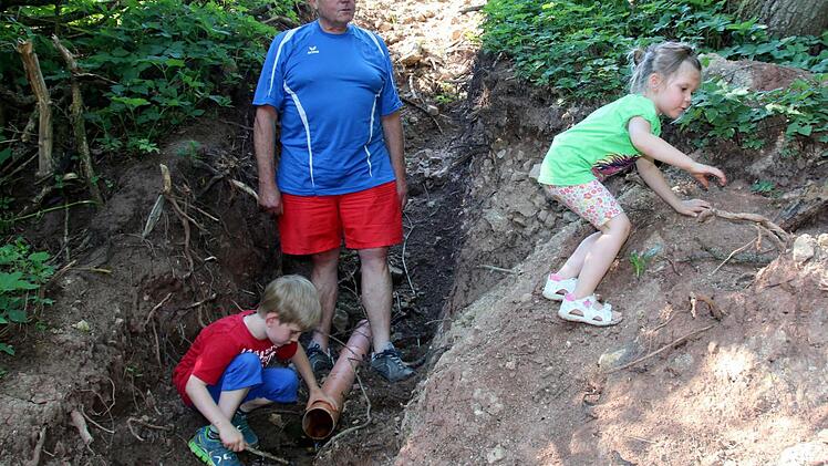 Die wiederentdeckte Heiligenquelle in der Gemündaer Flur, die Hermann Gossenberger hier seinen Enkeln Elena und Finn zeigt, kennen bisher nur wenige Eingeweihte. Noch rinnt das Wasser aus einem schmucklosen Plastikrohr. Auf Wunsch der "Stiftung 1150 Jahre Dorfgemeinschaft Gemünda" soll sich beides durch einen Gestaltungswettbewerb bald ändern.Foto: Bettina Knauth