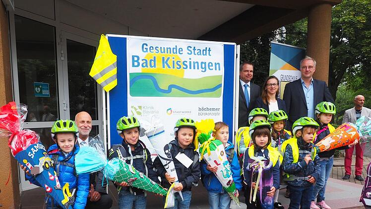 Fahrradhelme für ABC-Schützen (1): Oberbürgermeister Kay Blankenburg (h.l.) überreichte zusammen mit Mitgliedern des Expertenboards des "Gesunde Städte-Netzwerk" Bad Kissingen, hintere Reihe: Leiter des RSG Bad Kissingen Dr. Matthias Wagner (3.v.r.), vom RSG Bad Kissingen Nadine Menz (2.v.r.), rechts außen Rektor Bernd Czelustek, in der Henneberg-Grundschule Garitz Fahrradhelme und Sicherheitswesten an die ABC-Schützen.