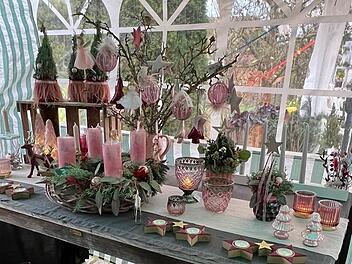 Ein weihnachtlich geschmückter Tisch mit rosa Kerzen, Sternen, Zweigen und Dekorationen. Ein Adventskranz und Kerzenhalter runden die festliche Szenerie ab.