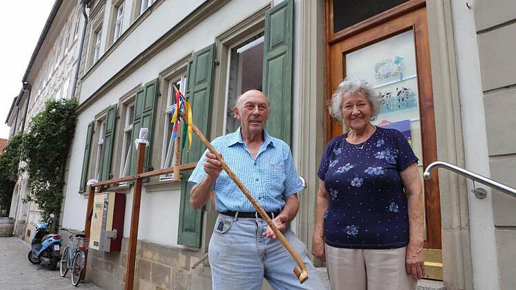 Adolf Koch zeigt den selbstgeschnitzen Dreschflegel. Die Kochs stehen vor der Tür des ehemaligen Tante-Emma-Ladens. Foto: Barbara Herbst