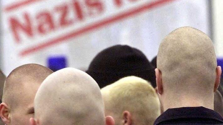 Mit kahlgeschorenen Köpfen stehen Teilnehmer einer Neonazi-Demo in Dortmund vor einem Plakat mit der Aufschrift "Nazis raus".  Foto: Archiv/dpa