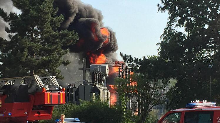 Feuer und dichter schwarzer Rauch ist am 04.07.2015 in Schweinfurt (Bayern) im abgesperrten Bereich einer Trafostation zu sehen. Nach einer Explosion in der Trafostation ist in Schweinfurt der Strom ausgefallen. Das Feuer konnte nach zwei Stunden gel&ouml;scht werden; auch die Stromversorgung in der 51 000-Einwohner-Stadt war am Mittag wiederhergestellt. Verletzt wurde niemand. Foto: Andr&eacute; Jurleit/dpa