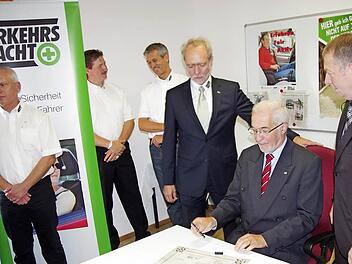 Regierungspräsident Paul Beinhofer unterzeichnet den Sicherheitsvertrag. Links daneben der Vorsitzende der Kreisverkehrswacht, Norbert Reiter, rechts Landrat Thomas Bold.  Fotos: Klaus Werner