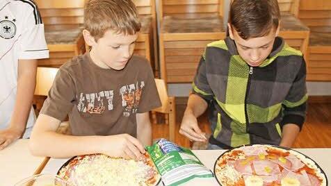 Leon (links) und Kevin sind ganz vertieft beim Belegen ihrer Pizzen.
