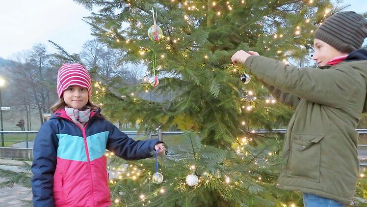 Theresa (7) und Finn (9) Ruppenstein haben mitgebastelt und schmücken mit ihren Kugeln den Baum am Kirchenvorplatz. Foto: Monika Schütz