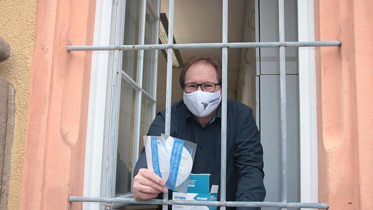 Auch wenn die Fenster des Hammelburger Pfarrbüros vergittert sind, kommen die Masken von Herzen: Pfarrer Thomas Eschenbacher bei der Ausgabe.  Foto: Ralf Ruppert