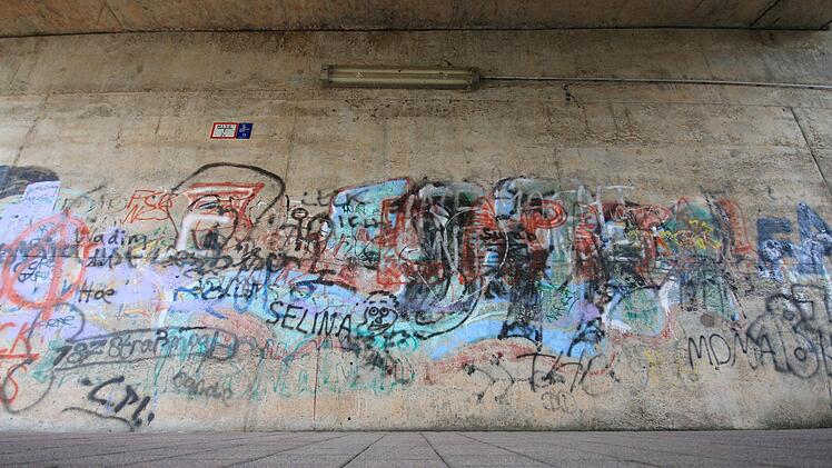 In der Unterführung an der Steinmauer in Garitz haben sich im Laufe der Zeit viele Sprayer verewigt.  Ruppert sieht die Wand als Schriftensammlung mit politischem Statement (links: das rote  A in einem Kreis als anarchistisches Symbol).  "Sieht man alles als fertig an, würde ich es als Schmiererei einordnen", sagt er. Allerdings gefällt ihm die Farbkomposition. Die Wand könnte höchstens als Untergrund für eine weitere bildliche Darstellung dienen.   Foto: Benedikt Borst