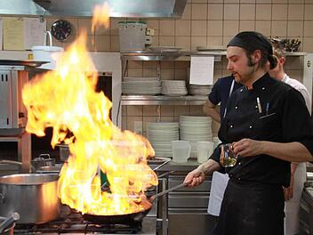 Wenn Männer kochen, muss schon mal der eine oder andere zündende Spezialeffekt dabei sein: Hier zeigt Rico Pfitzner den Kursteilnehmern, wie Steaks mit Calvados flambiert werden - für derart spektakuläre Aktionen ist eine Restaurantküche wohl geeignet, aber längst nicht jede Kochnische. Außer solchen spektakulären Bildern gab's an diesem Abend jede Menge "Versucherla" für die Hobbyköche. Foto: Matthias Einwag