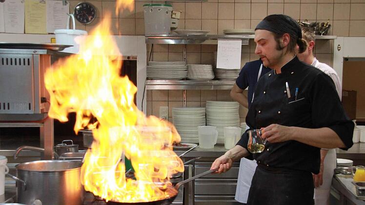 Wenn Männer kochen, muss schon mal der eine oder andere zündende Spezialeffekt dabei sein: Hier zeigt Rico Pfitzner den Kursteilnehmern, wie Steaks mit Calvados flambiert werden - für derart spektakuläre Aktionen ist eine Restaurantküche wohl geeignet, aber längst nicht jede Kochnische. Außer solchen spektakulären Bildern gab's an diesem Abend jede Menge "Versucherla" für die Hobbyköche. Foto: Matthias Einwag