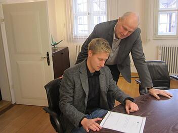 David Spenger (links) &uuml;bergibt B&uuml;rgermeister Gerald Brehm einen Abzug seiner Bachelorarbeit, die sich mit dem Karpfenland besch&auml;ftigt.  Foto: Filiz Mailhammer