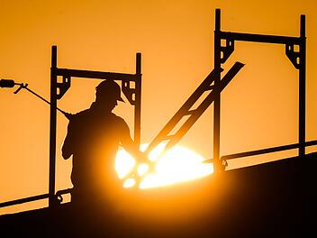 Ein Bauarbeiter im Gegenlicht der Sonne auf einem Ger&uuml;st