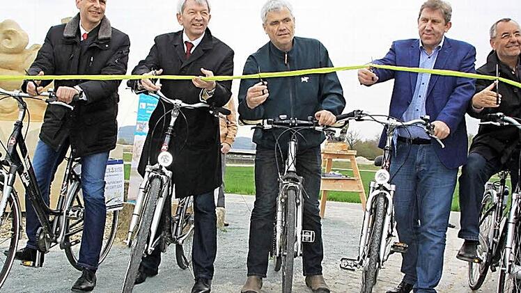 Das Eröffnungsband des Auenwegs, der die Kreise Lichtenfels und Bamberg verbindet, schneiden Politiker aus beiden Kreisen gemeinsam durch (von links): Landrat Christian Meißner (Lichtenfels), Landrat Hans Kalb (Bamberg), Bürgermeister Bernhard Storath (Ebensfeld), MdB Andreas Schwarz und Bürgermeister Jürgen Kohmann (Bad Staffelstein). Anschließend radelten sie die ersten 1,5 Kilometer bis nach Niederau. Foto: Matthias Einwag