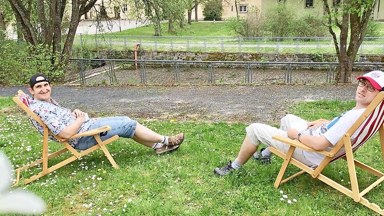 Zwei Bewohner im Dominikus-Ringeisen-Werk Maria Bildhausen genießen schon einmal bei den Vorbereitungen für den Bildhäuser Strand den Ausblick über den Bildhäuser Weiher in den Klosterpark.