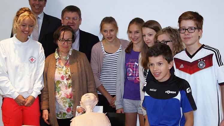 Inga Hoffmann, Koordinatorin des Schulsanitätsdienstes Rhön-Gymnasium Bad Neustadt; Jochen Bocklet, Geschäftsführer Rhön-Klinikum Campus Bad Neustadt; Edith Degenhardt, Schulleiterin Rhön-Gymnasium Bad Neustadt; Dr. med. Michael Dinkel, Chefarzt der Klinik für Anästhesie und Intensivmedizin Bad Neustadt mit Schülern des Rhön-Gymnasiums und eine der 20 übergebenen Reanimationspuppen Foto: Rhön-Klinikum
