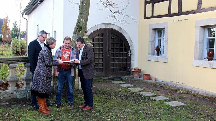 Kerstin Blum und Bürgermeister Fischkal schauen mit Siggi Kraus das Geschenk (Adelsdorf Chronik) an, dahinter links Wolfgang Mößlein - im Hintergrund die Scheune  Fotos: Johanna Blum