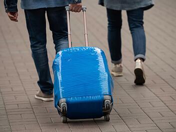 A man carries a suitcase wrapped in blue film