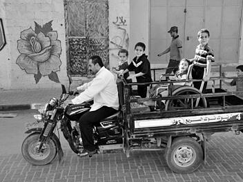 Ein Vater transportiert seine Kinder, darunter einen Jungen im Rollstuhl, durch die Straßen irgendwo im Gaza. Foto: Till Mayer